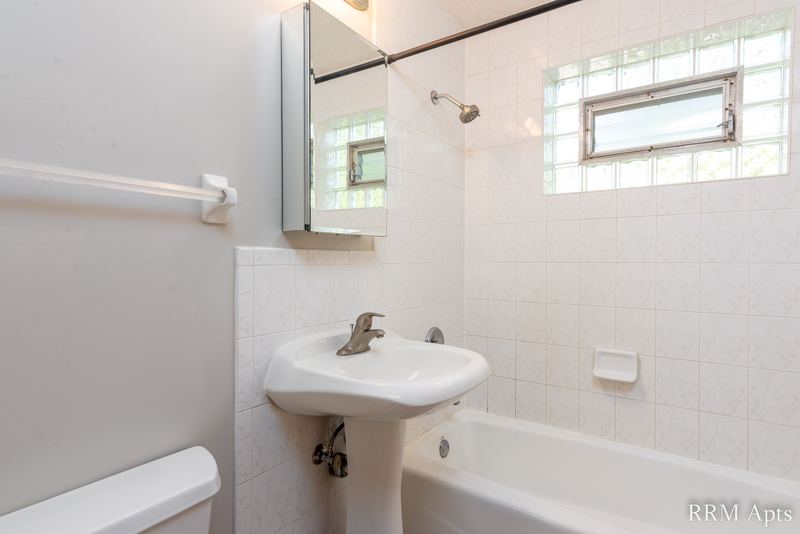 Bathroom with white tile walls, glass block window, pedestal sink, mirrored cabinet and tub, Park Avenue apartment 607 203