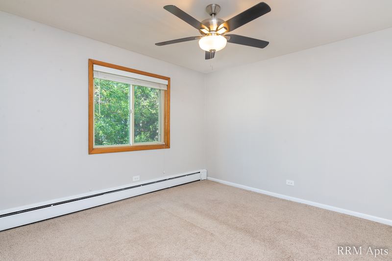Bedroom with beige carpet, ceiling fan, gray walls and an oak-trimmed window with trees, Park Avenue apartment 607 203
