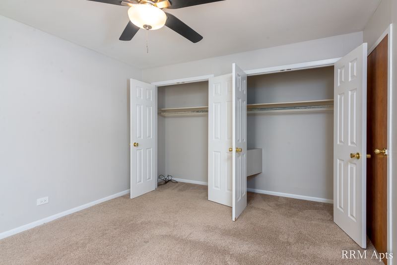 Bedroom with beige carpet, ceiling fan, two open closets with shelves and an oak door, Park Avenue apartment 607 203