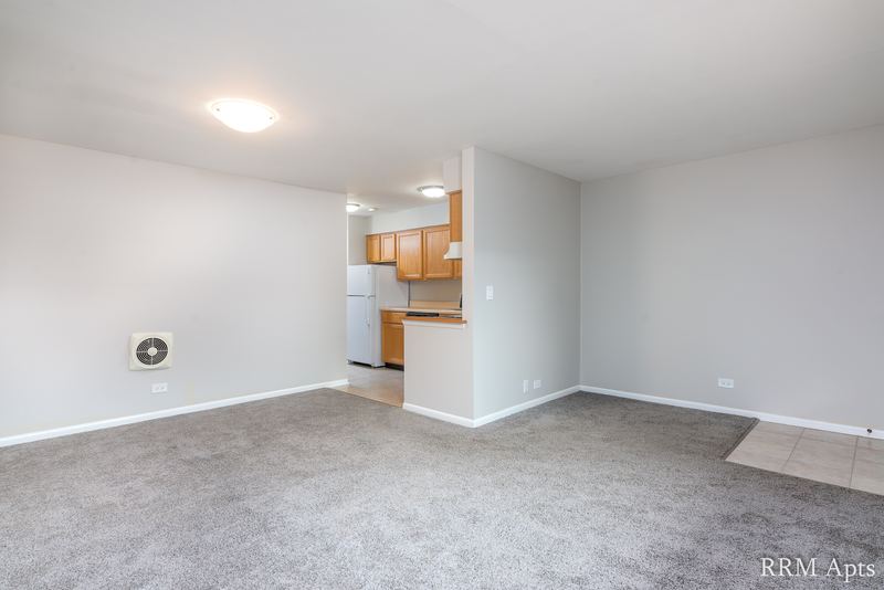 Living room with gray carpet, a round wall vent and a view into the oak-cabinet kitchen, Park Avenue apartment 607 204