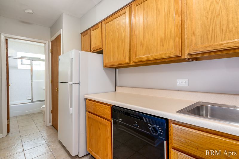 Kitchen with oak cabinets, white refrigerator, black dishwasher and a hall to the bathroom, Park Avenue apartment 607 204