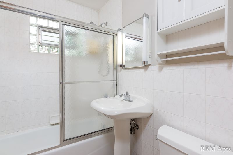 Bathroom with white tile walls, sliding glass tub doors, pedestal sink and mirrored cabinet, Park Avenue apartment 607 204