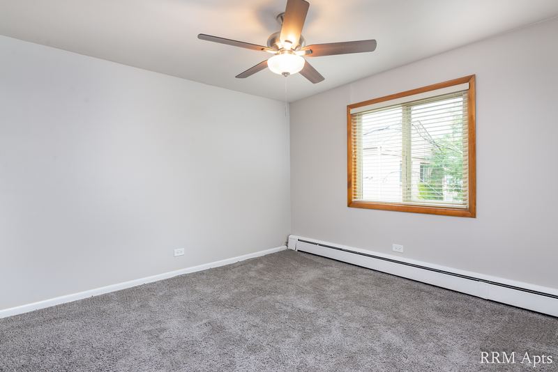 Bedroom with gray carpet, ceiling fan, oak-trimmed window with trees and a baseboard heater, Park Avenue apartment 607 204