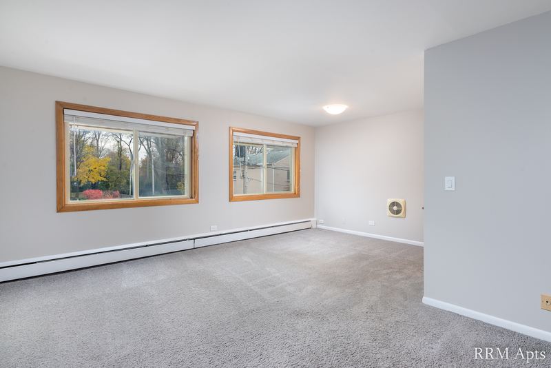 Living room with gray carpet, two oak-trimmed windows with trees and a baseboard heater, Park Avenue apartment 607 206