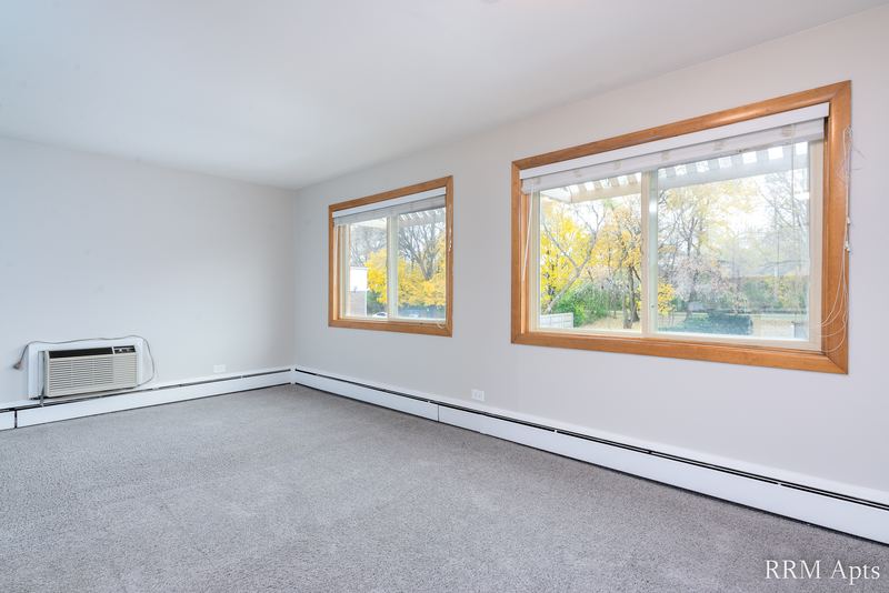Living room with gray carpet, two windows with autumn trees and a wall air conditioner, Park Avenue apartment 607 206