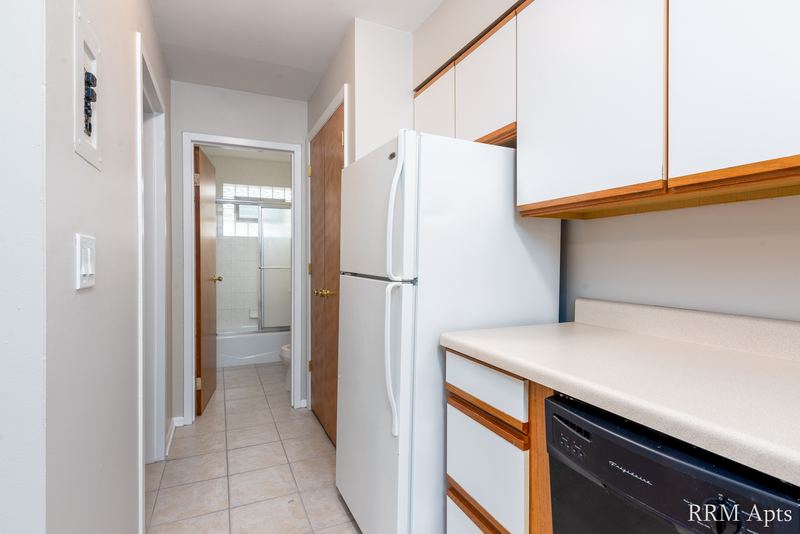 Kitchen with white oak-trimmed cabinets, white refrigerator, black dishwasher and a hallway, Park Avenue apartment 607 206