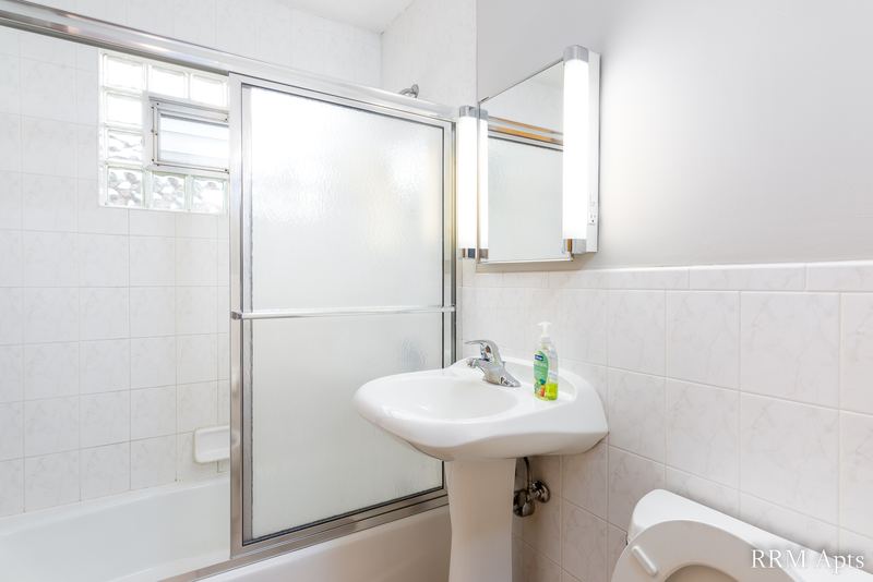 Bathroom with white tile walls, glass tub doors, glass block window and a pedestal sink, Park Avenue apartment 607 206