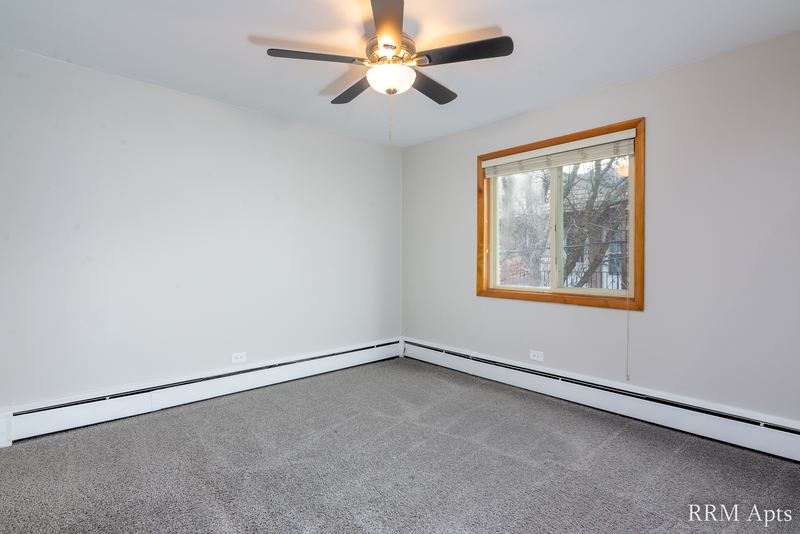 Bedroom with gray carpet, ceiling fan, gray walls and an oak-trimmed window with trees, Park Avenue apartment 607 206