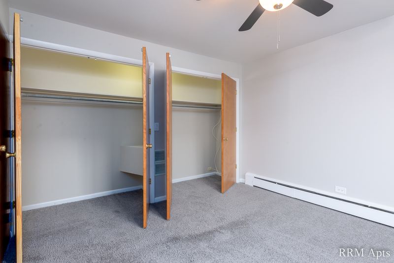 Bedroom with gray carpet, ceiling fan, open closets with oak doors and a baseboard heater, Park Avenue apartment 607 206