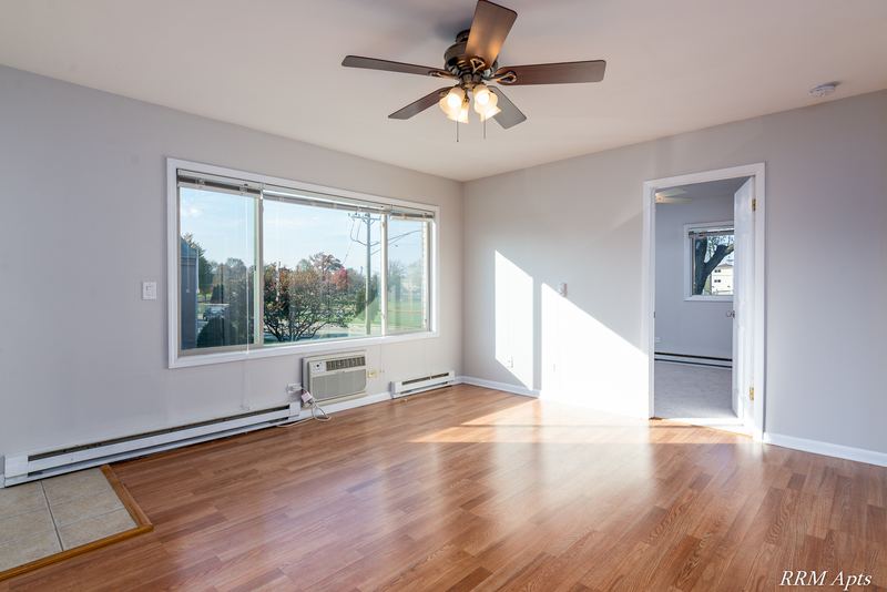 Living room with wood floor, ceiling fan, window with trees and a wall air conditioner, Park West apartment 611 C