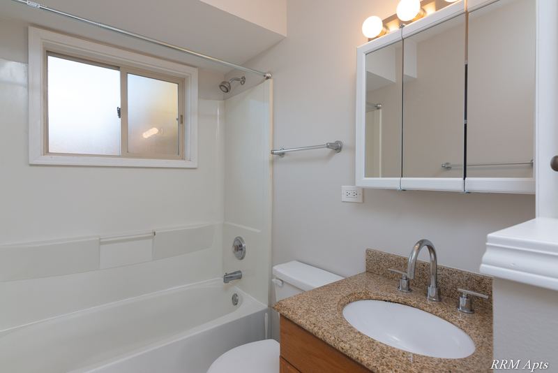 Bathroom with white tub, frosted window, mirrored medicine cabinet and granite-look vanity, Park West apartment 611 C