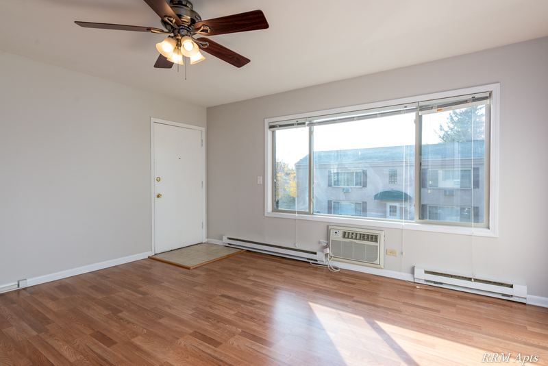 Living room with wood floor, ceiling fan, entry door and a wide window facing the next building, Park West apartment 611 C