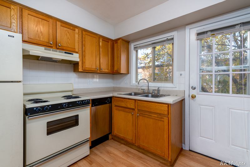 Kitchen with oak cabinets, white stove and refrigerator, sink window and a glass-paned door, Park West apartment 611 C