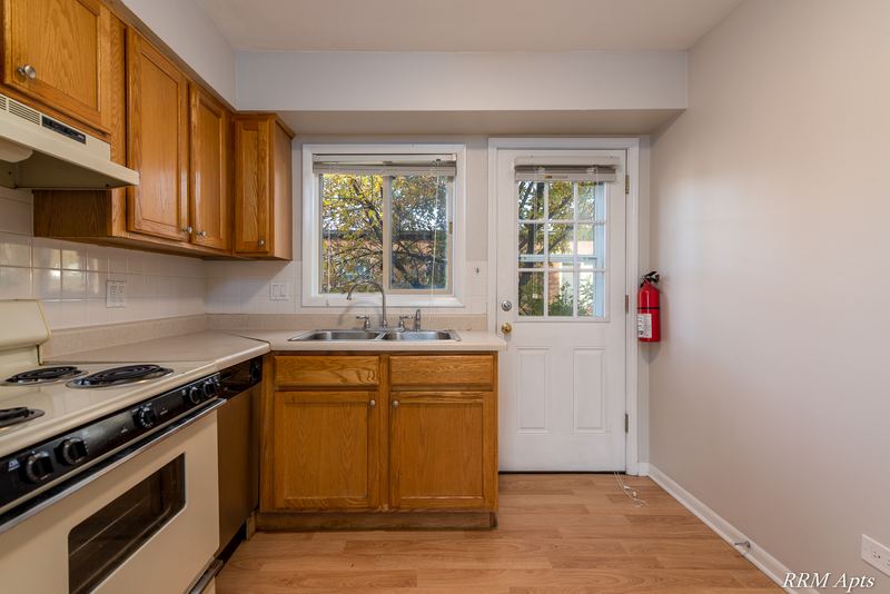 Kitchen with oak cabinets, white stove, wood floor and a glass-paned door beside the sink window, Park West apartment 611 C