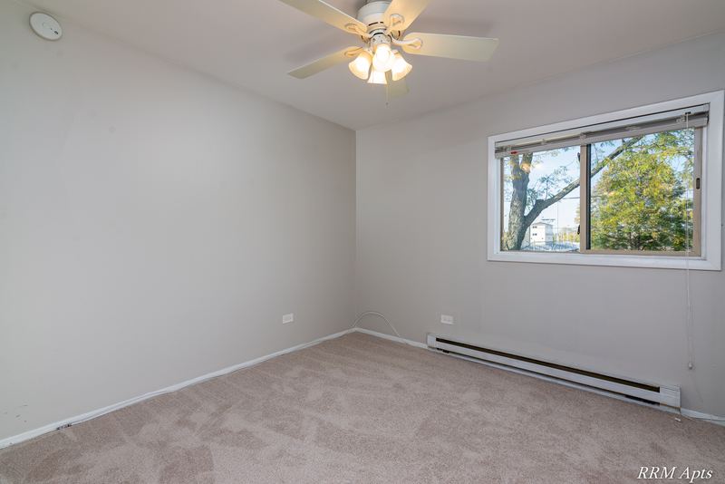 Bedroom with beige carpet, ceiling fan, window with trees and a baseboard heater, Park West apartment 611 C