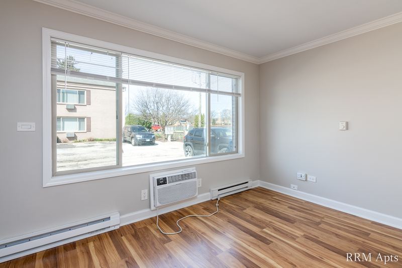 Living room with wood floor, wide window facing the next building and a wall air conditioner, Park West apartment 611A