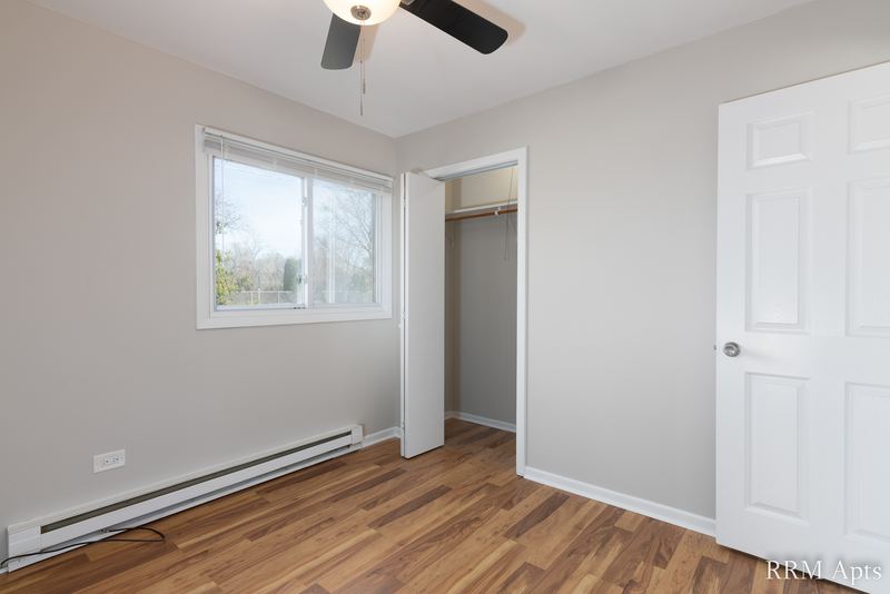 Bedroom with wood floor, ceiling fan, window, open closet and a white door, Park West apartment 611A