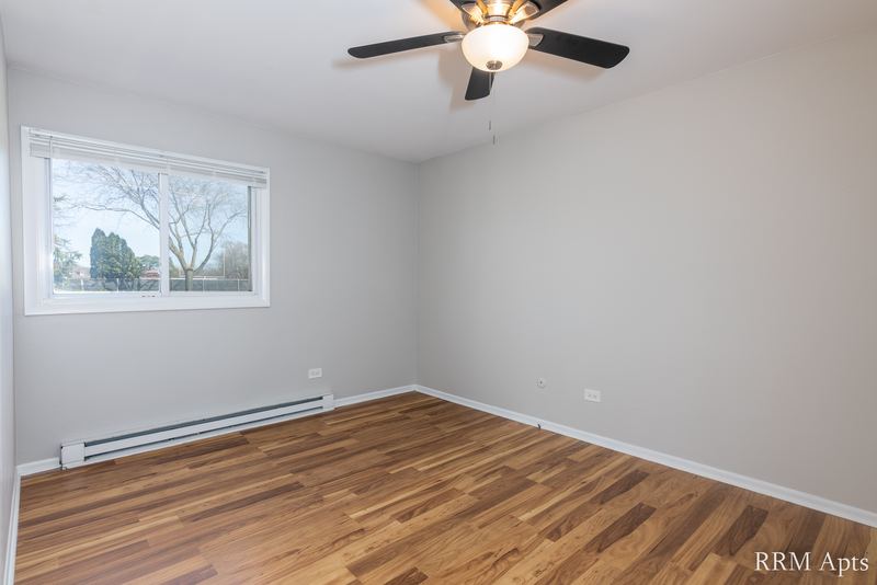 Bedroom with wood floor, ceiling fan, gray walls and a window with trees, Park West apartment 611A