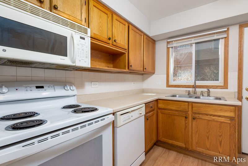 Kitchen with oak cabinets, white stove, microwave and dishwasher, and a window over the sink, Park West apartment 611A