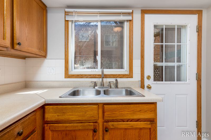 Kitchen with oak cabinets, double sink under a window with trees and a glass-paned door, Park West apartment 611A