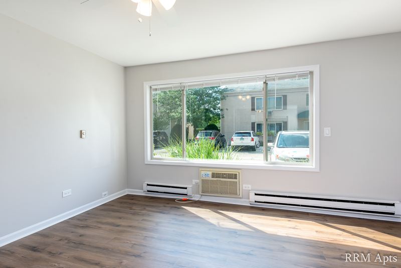Living room with wood-look floor, wide window over the parking lot and a wall air conditioner, Park West apartment 613 B