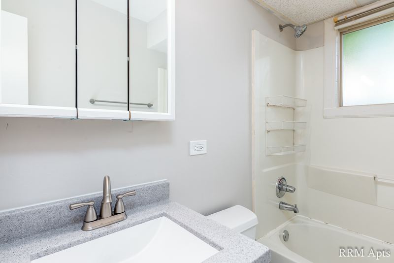 Bathroom with white tub, small window, mirrored medicine cabinet and gray granite-look vanity, Park West apartment 613 B