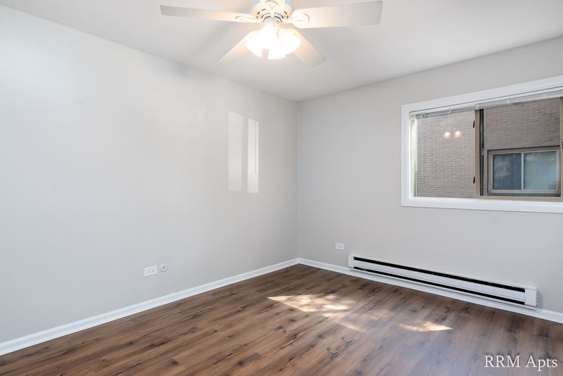 Bedroom with wood-look floor, ceiling fan, window facing a brick wall and a baseboard heater, Park West apartment 613 B