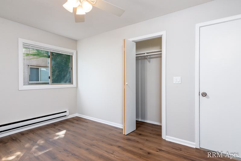 Bedroom with wood-look floor, ceiling fan, window, open closet and a white door, Park West apartment 613 B