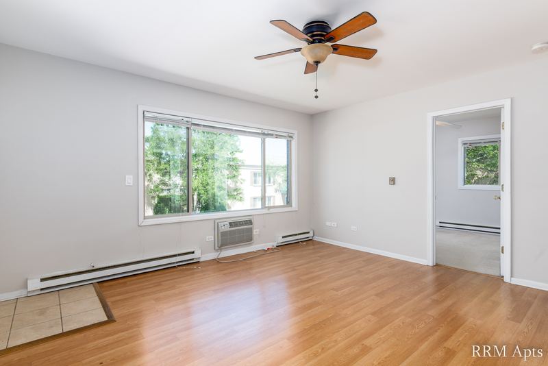 Living room with wood floor, wide window with trees, wall air conditioner and a tile entry, Park West apartment 613 C