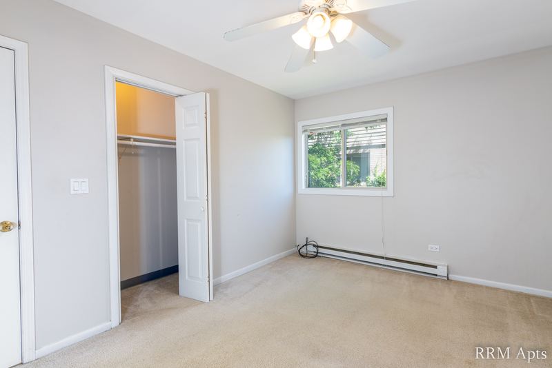Bedroom with beige carpet, ceiling fan, open bifold closet and a window with trees, Park West apartment 613 C