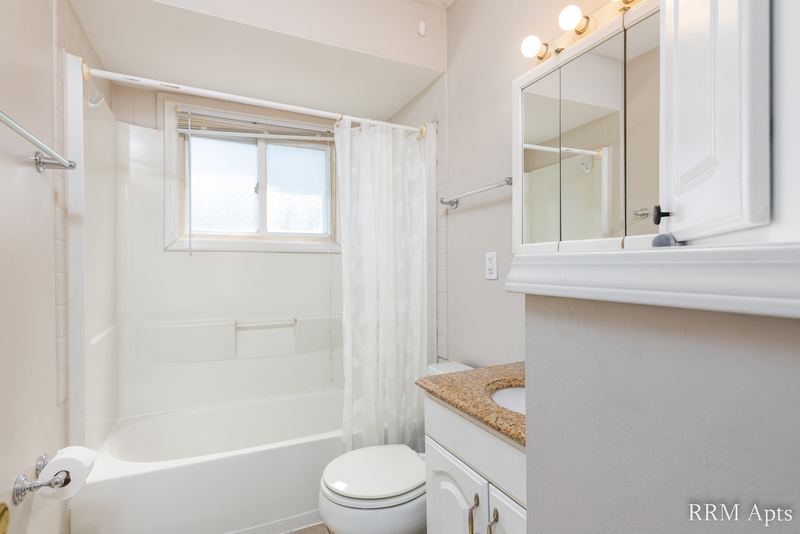 Bathroom with white tile tub surround, window, mirrored cabinet and granite-look vanity, Park West apartment 613 C