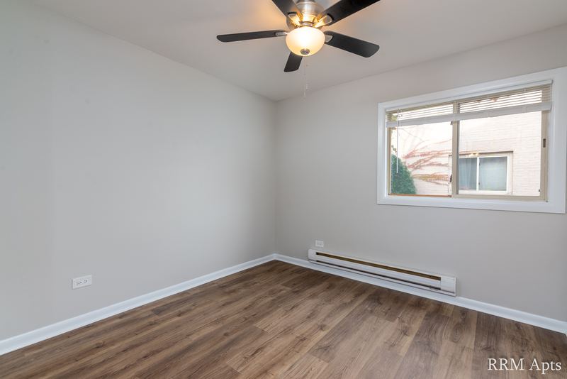 Bedroom with wood-look floor, ceiling fan, window facing a brick wall and a baseboard heater, Park West apartment 615 A