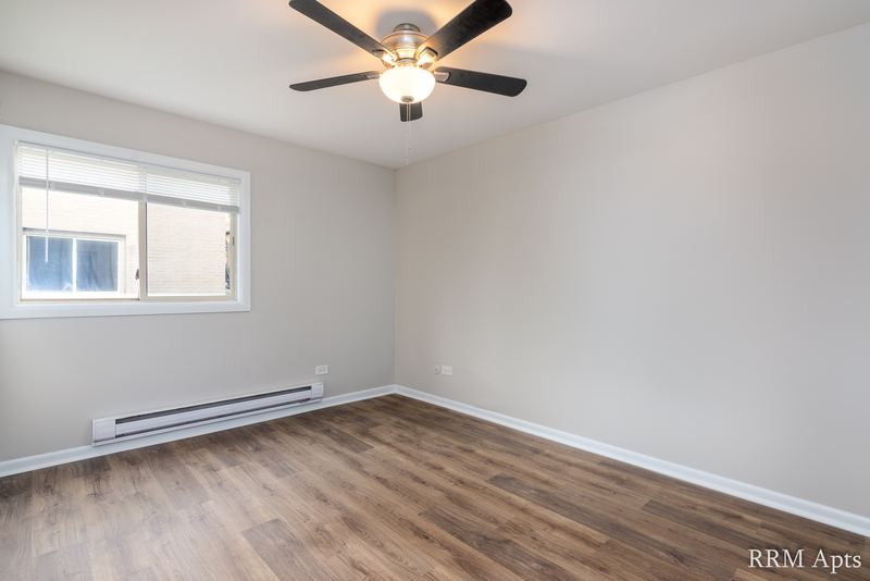 Bedroom with wood-look floor, ceiling fan, gray walls and a window with a brick wall outside, Park West apartment 615 A