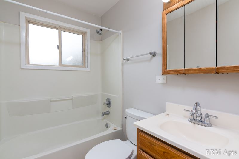 Bathroom with white tub, small window, oak-trimmed mirrored cabinet and oak vanity, Park West apartment 615 A