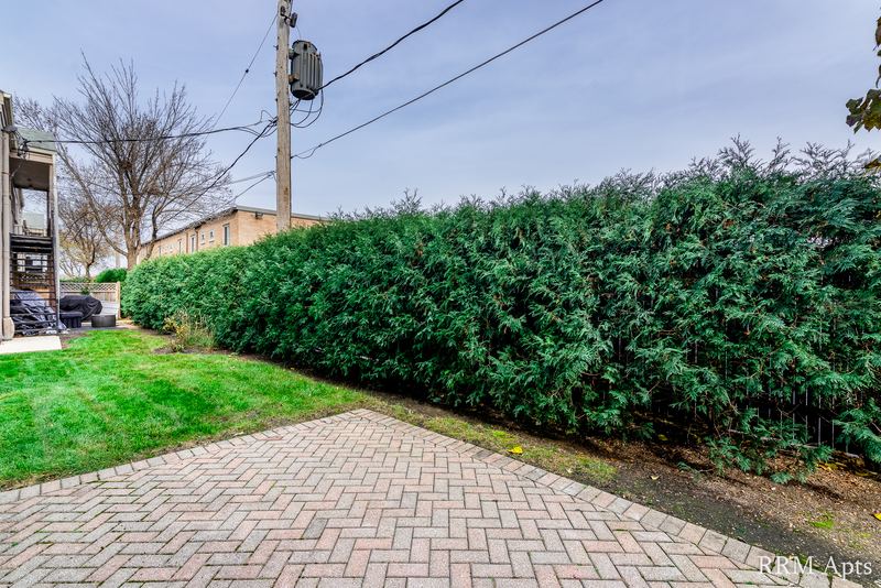 Patio with brick pavers, a strip of lawn, tall hedge and a view of the next building, Park West apartment 615 A