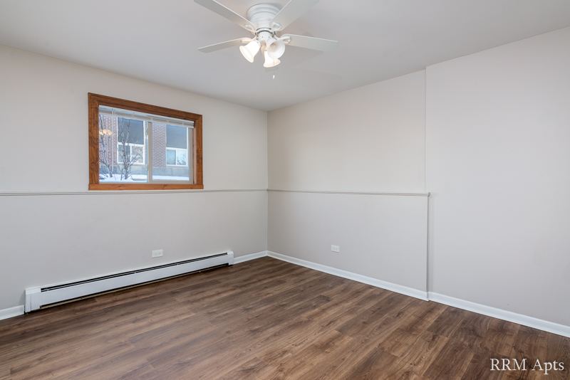 Living room with ceiling fan, window, baseboard heater and wood-look floor, Pioneer Court apartment 900-1A