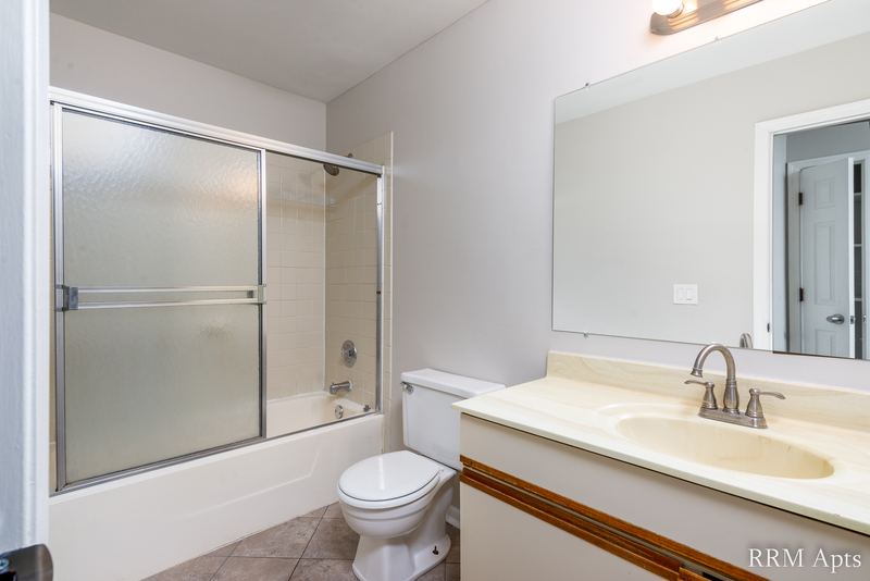 Bathroom with sliding glass tub doors, oak-trimmed vanity and a wide mirror, Pioneer Court apartment 900 1D