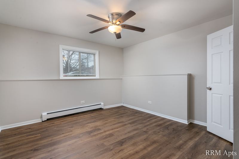 Bedroom with wood-look floor, ceiling fan, window with trees and a white door, Pioneer Court apartment 900 1D