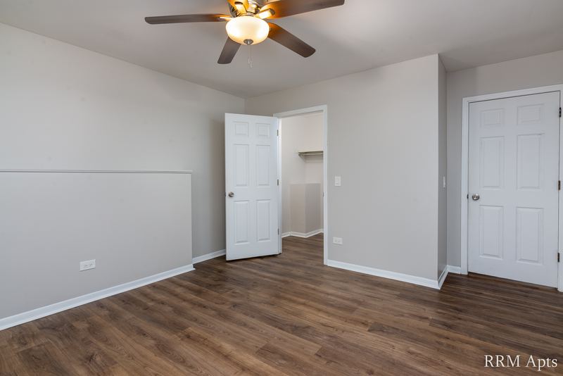 Bedroom with wood-look floor, ceiling fan, open door to the hall and a white closet door, Pioneer Court apartment 900 1D
