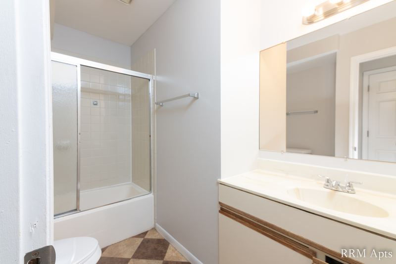 Bathroom with sliding glass tub doors, tile floor, oak-trimmed vanity and a wide mirror, Pioneer Court apartment 900 2A