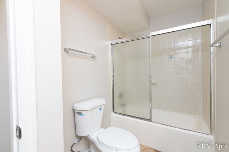 Bathroom with sliding glass tub doors, white tile surround, toilet and a towel bar, Pioneer Court apartment 900 2A