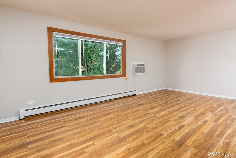 Living room with wood-look floor, oak-trimmed window with trees and a wall air conditioner, Pioneer Court apartment 900 2E