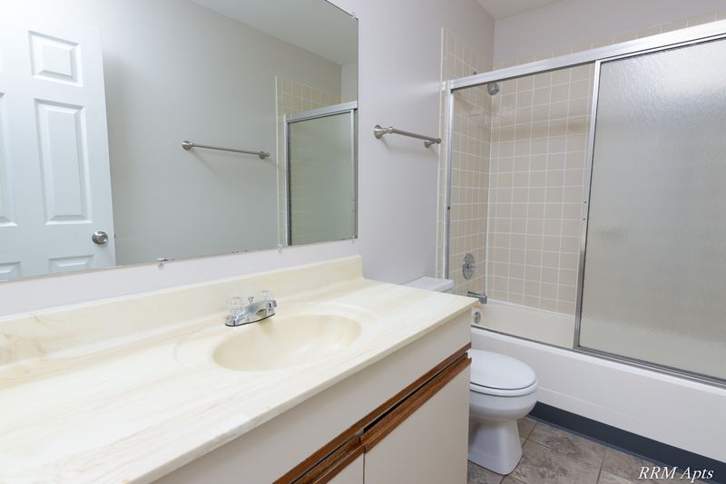 Bathroom with cream vanity, wide mirror, sliding glass tub doors and a white door, Pioneer Court apartment 900 2E