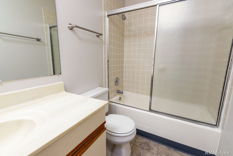 Bathroom with tan tile tub surround, sliding glass doors, cream vanity and toilet, Pioneer Court apartment 900 2E
