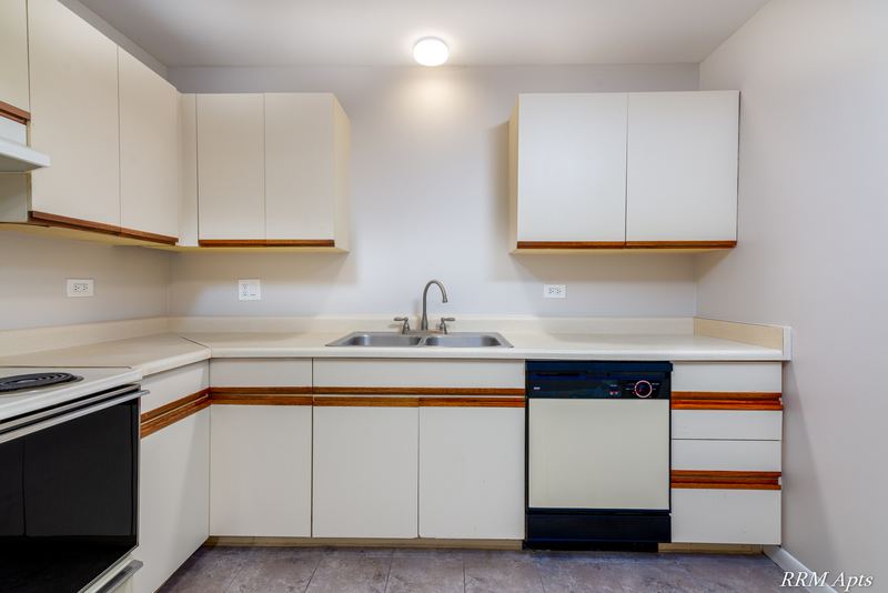 Kitchen with white oak-trimmed cabinets, black stove, white dishwasher and a double sink, Pioneer Court apartment 900 2E
