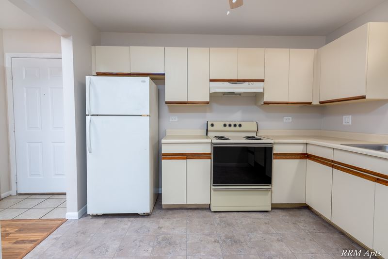 Kitchen with white oak-trimmed cabinets, white refrigerator, black stove and a white door, Pioneer Court apartment 900 2E