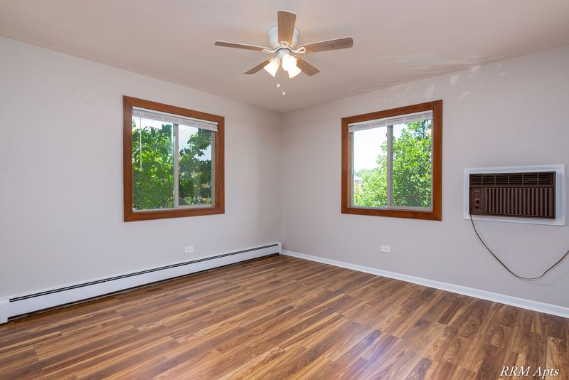 Bedroom with wood-look floor, ceiling fan, two windows with trees and wall air conditioner, Pioneer Court apartment 900 2E