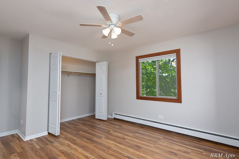 Bedroom with wood-look floor, ceiling fan, open closet and a window with trees, Pioneer Court apartment 900 2E