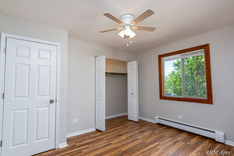 Bedroom with wood-look floor, ceiling fan, white door, open closet and a window with trees, Pioneer Court apartment 900 2E