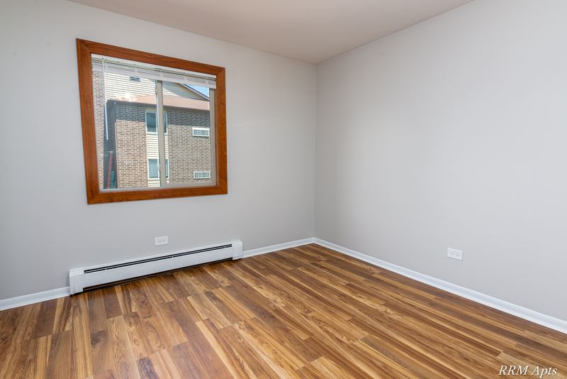 Bedroom with wood-look floor, window facing a brick building and a baseboard heater, Pioneer Court apartment 900 2E